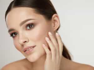 Beautiful Girl Caressing Facial Skin Posing On Grey Background.