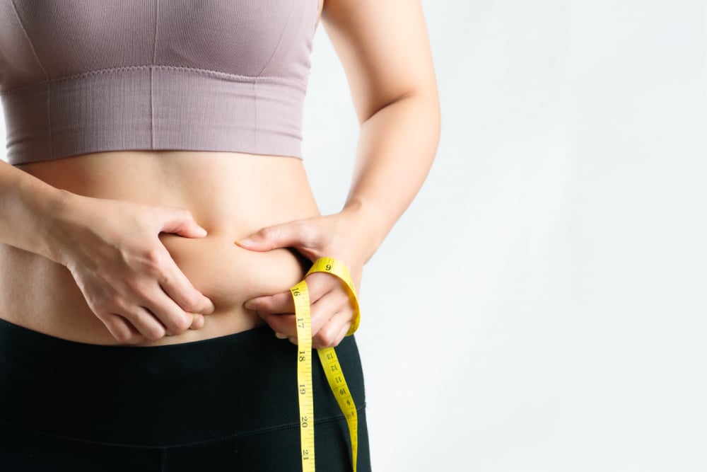 A woman starting the hCG diet pinching her stomach while holding a tape measure